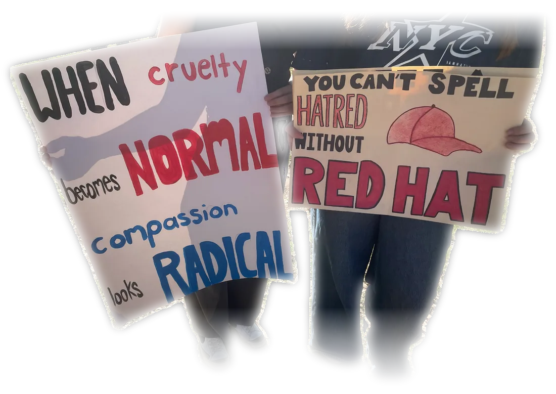 Two people holding hand-painted protest signs: "When cruelty becomes normal, compassion looks radical" and "You can't spell hatred without red hat."